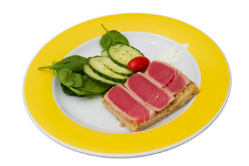 Seared ahi tuna with cucumber salad on a white and yellow plate isolated on white
