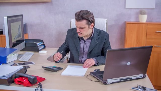 A businessman is calculating something and then he is writing things down on a piece of paper.
