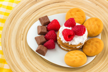 Fresh Red Raspberries on a white artistic plate / Red Fresh Raspberries on a white artistic plate with cookies, rosemary, chocolate and cream in the background.