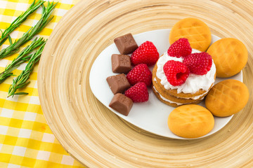 Fresh Red Raspberries on a white artistic plate / Red Fresh Raspberries on a white artistic plate with cookies, rosemary, chocolate and cream in the background.