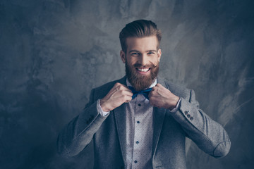Happy young happy bearded man with mustache in formalewear stands on a gray background and holds...