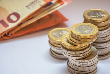 gestapelte Euromünzen mit Geldscheinen im Hintergrund