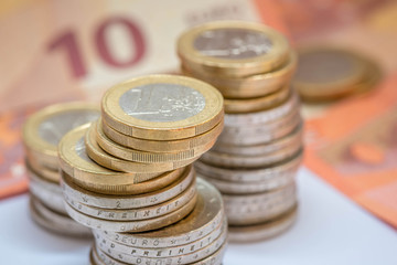 gestapelte Euromünzen mit Geldscheinen im Hintergrund