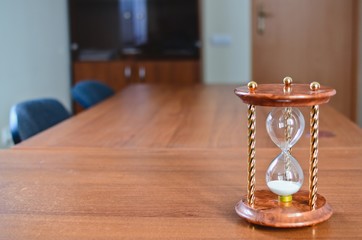 A sand timer (hourglass) on the wooden office desk(table).Copy space