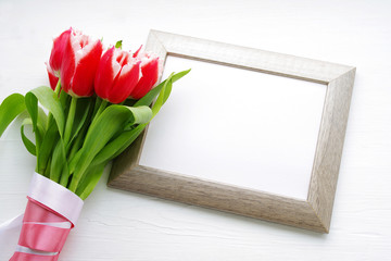 Bouquet of red tulips and a frame with white space for your text on a light wooden surface. Festive flower background by a Mother's Day or other celebration