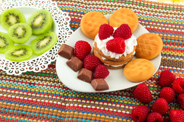 Fresh Red Raspberries on a white artistic plate / Red Fresh Raspberries on a white artistic plate with cookies, rosemary, chocolate and cream in the background.