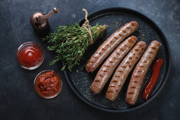 Frying pan with barbecued marbled beef sausages, fresh thyme and sauces, high angle view