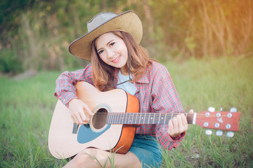 portrait of a happy young woman asia playing guitar outdoors