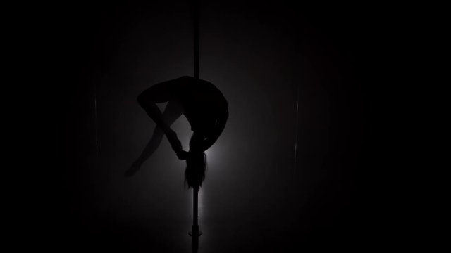 Young woman's silhouette dancing on the pole in smoke