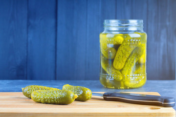 Cucumbers or pickled gherkins with a knife on a wooden cutting board. Blue gray background. Bank with cucumbers.