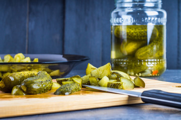 Cucumbers or pickled gherkins with a knife on a wooden cutting board. Blue gray background. Bank with cucumbers.
