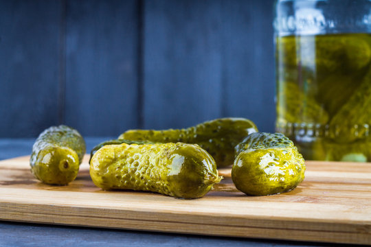 Cucumbers or pickled gherkins with a knife on a wooden cutting board. Blue gray background. Bank with cucumbers.