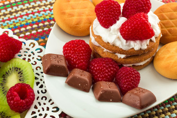 Fresh Red Raspberries on a white artistic plate / Red Fresh Raspberries on a white artistic plate with cookies, rosemary, chocolate and cream in the background.