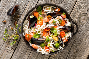 Cast iron pan with rice noodles and mussels. Fresh tasty food.