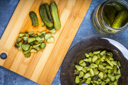 Cucumbers or pickled gherkins with a knife on a wooden cutting board. Blue gray background. Bank with cucumbers.