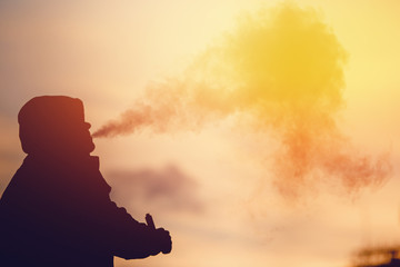 Close-up A man vape smokes an electronic cigarette against the sunset. The steam is falling. Concept Abandonment of tobacco. high contrast and monochrome color tone.