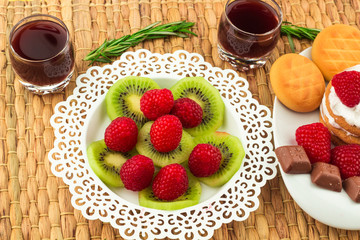 Fresh Red Raspberries on a white artistic plate / Red Fresh Raspberries on a white artistic plate with cookies, rosemary, chocolate and cream in the background.