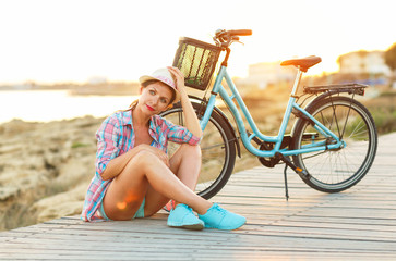 Carefree woman with bicycle sitting on a wooden path at the sea