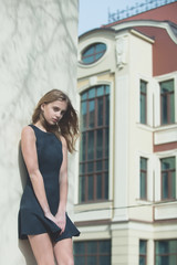Fototapeta premium Pretty girl in fashionable black dress at building wall