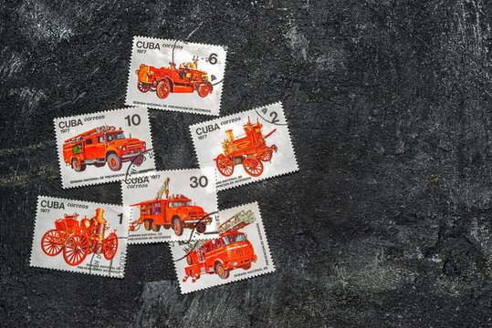 Moscow, Russia - April 20, 2017: Set of randomly lying postage stamps printed in Cuba shows fire engines, series, circa 1977. Copy space for your text on a dark black cement background.