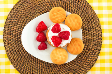 Fresh Red Raspberries on a white artistic plate / Red Fresh Raspberries on a white artistic plate with cookies, rosemary, chocolate and cream in the background.