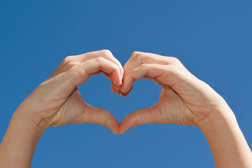 Hands making a heart shape against a blue sky
