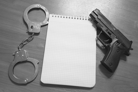Handgun handcuffs and notepad on the table with copy space black and white photography