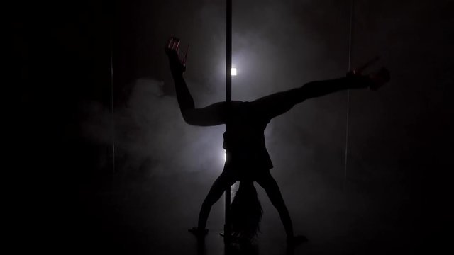 Young slim woman's silhouette in the skirt dancing near the pole upside down