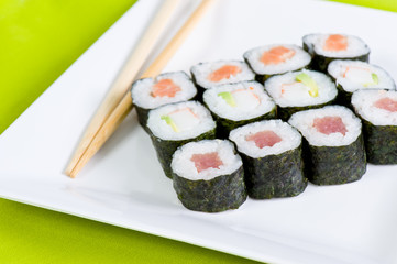 Tuna and salmon sushi rolls with chopsticks on a white plate on a green mat