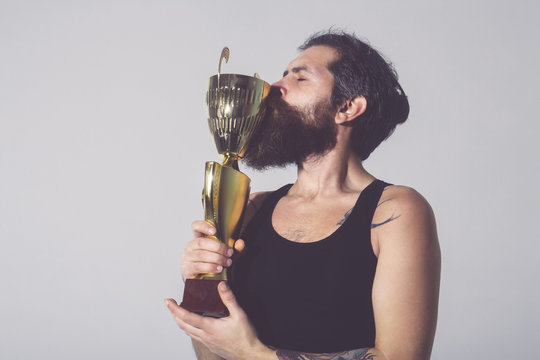 bearded happy man kissing gold champion cup on grey background