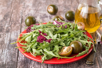 
Green salad.  Fresh green salad with tomatoes on a red plate, next to a glass jug with olive oil.
