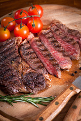 Sliced medium rare grilled Beef steak Ribeye with cherry tomatoes on cutting board, selective focus