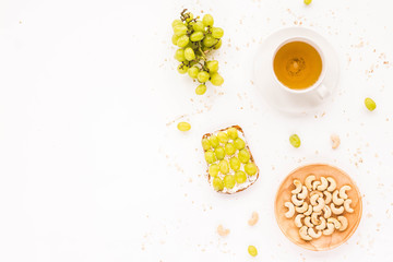 Healthy fruit breakfast. Cup of green tea, fruit toasts with grapes, cream cheese, berry, cereals and nuts on white background. Top view, flat lay.