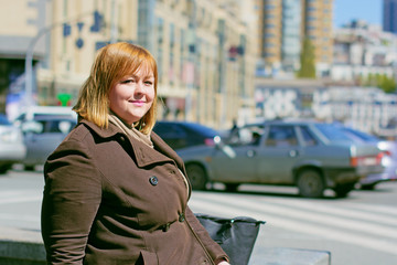 Obraz premium Pretty big woman of size plus size walks in the city, enjoys a sunny day and good weather in the rhythm of a big city life, cars and roads finds happiness in every day