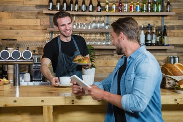 Waiter serving coffee to male customer at counter