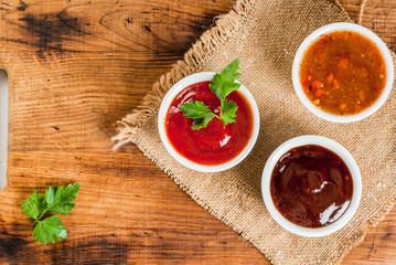 Three kinds of red tomato sauce on a wooden cutting board: traditional classic ketchup, barbecue sauce, sweet and sour Chinese sauce. Top view copy space