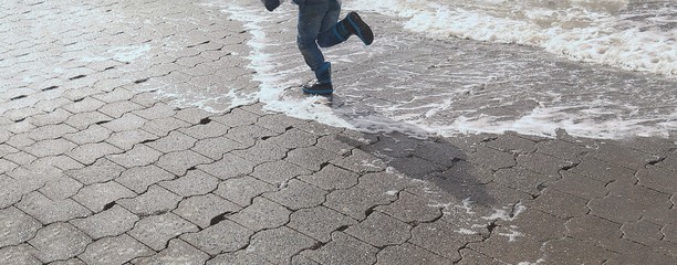 Kind mit Gummistiefeln läuft am Meer