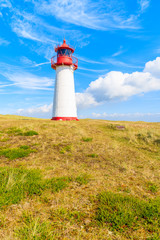 Lighthouse on sand dune against blue sky with white clouds on northern coast of Sylt island near List village, Germany