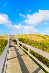 Fototapeta na wymiar Wooden walkway along a coast of North Sea and view of beautiful beach near Wenningstedt village, Sylt island, Germany