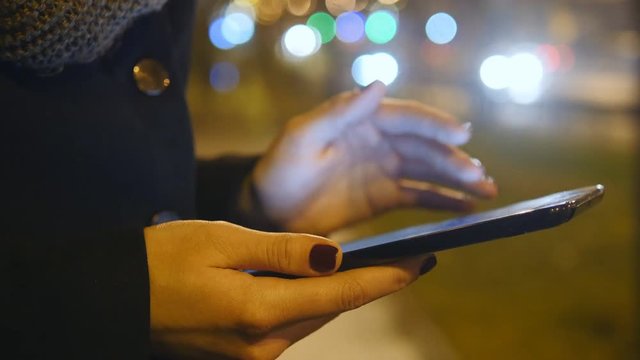 Young girl using tablet pc outdoors in the city at night. Beautiful blur night city traffic at background. Close up