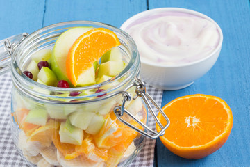Various fruits in a glass jar with yogurt and orange on a wooden table