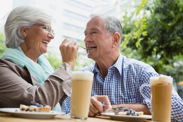 Senior woman feeding tart to man in café