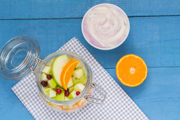 Various fruits in a glass jar with yogurt and orange on a wooden table