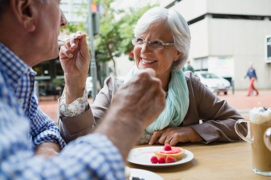 Senior woman feeding sweet food to man in café