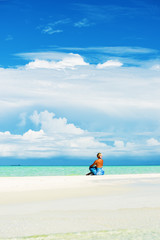 Obraz premium Blonde woman sitting on white sand beach, looking at open sea.Copy space