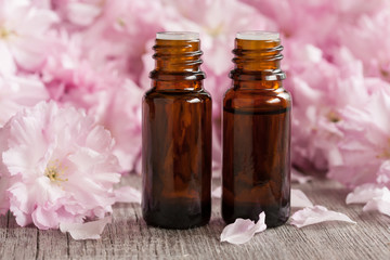 Two bottles of essential oil with pink japanese cherry blossoms in the background