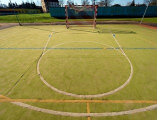 Empty outdoor handball playground, plastic hairy green surface on ground and white blue bounds lines.