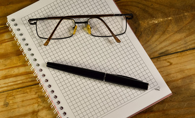 Fountain pen, glasses, and notebook on the wooden table