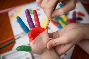 Young woman painting hands of little girl