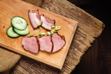 A close-up of sliced beef steak with a cucumber on a cutting board on a wooden background